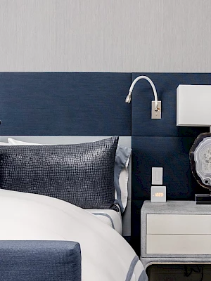 A modern bedroom with a stylish bed, blue headboard, and a neatly arranged bedside table featuring a lamp and decorative items.
