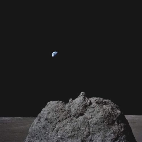 The image shows a view from the lunar surface with Earth visible above a rocky horizon against a dark sky.