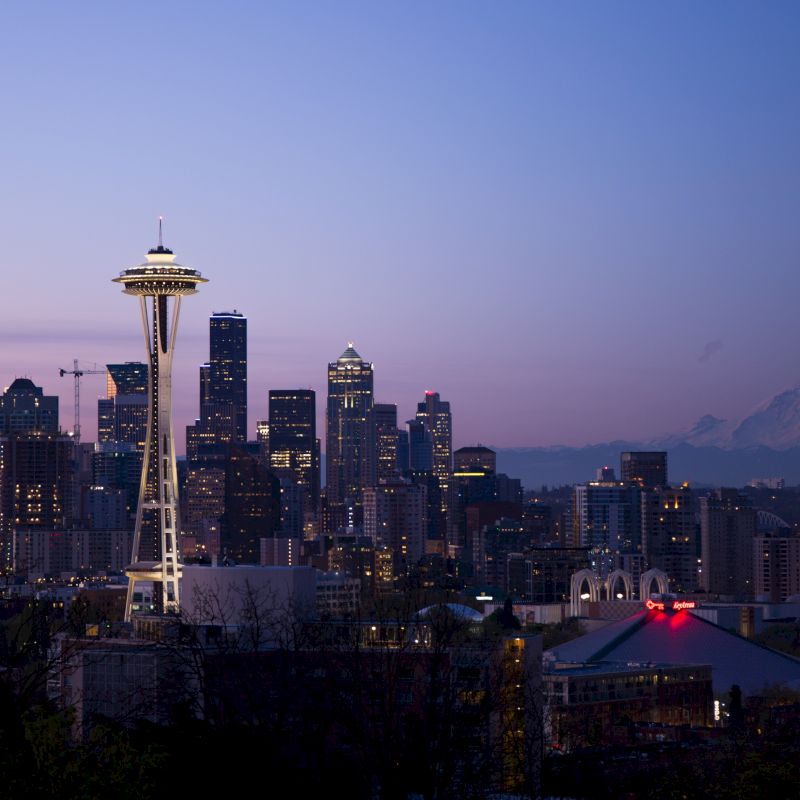 A twilight view of Seattle's skyline features the Space Needle, with Mount Rainier visible in the background.