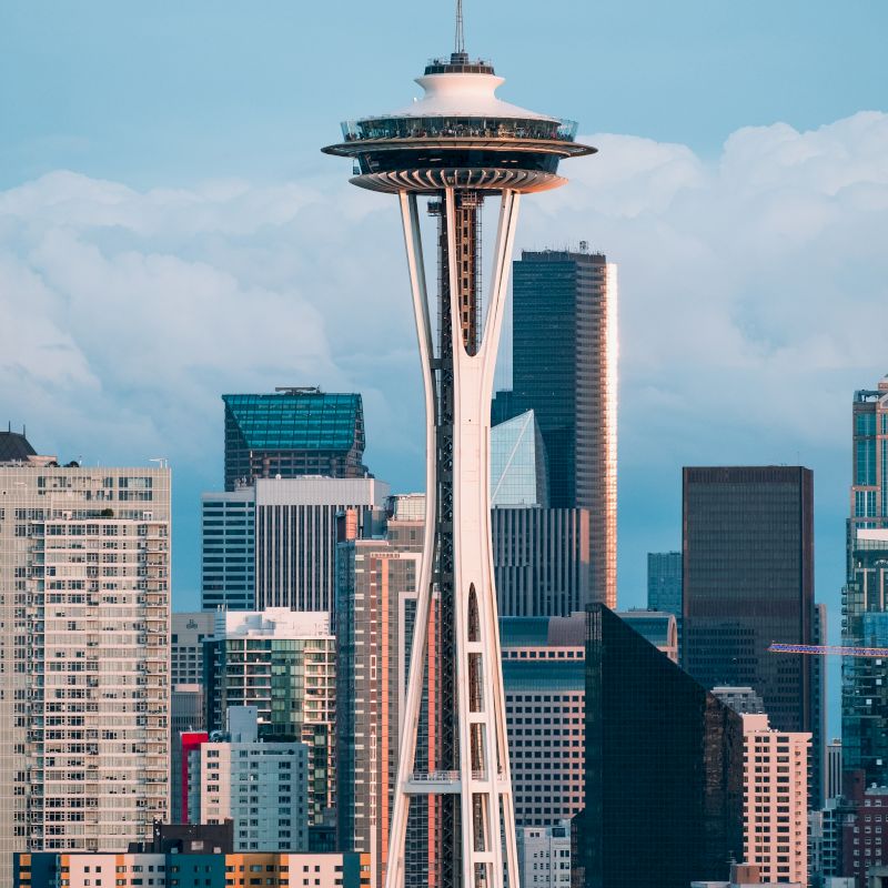The image shows the Seattle skyline with the Space Needle in the foreground, surrounded by modern skyscrapers under a cloudy sky.